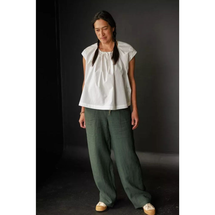 Woman wearing a white top and green pants against a dark background
