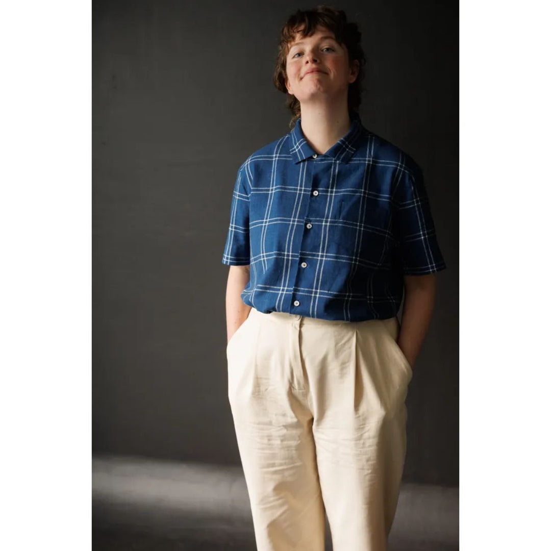 Person wearing a blue plaid shirt and beige pants against a dark background
