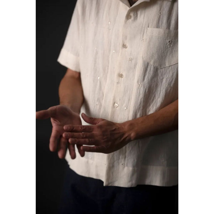 Person wearing a white button-up shirt with dark sleeves and pants, holding hands together.