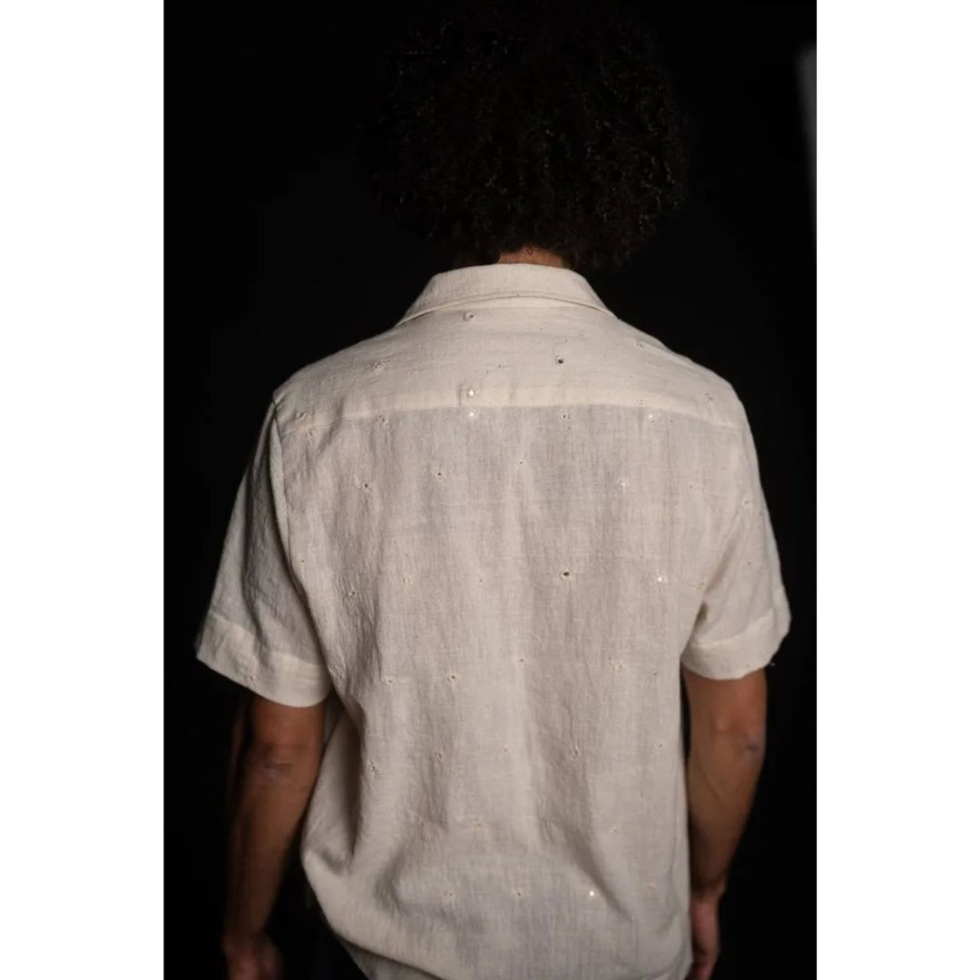 Person wearing a light-colored short-sleeve shirt with subtle patterns on a dark background