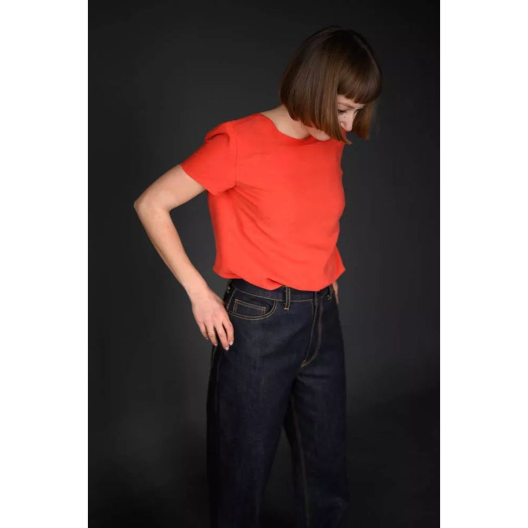 Person wearing a red top and dark jeans against a black background