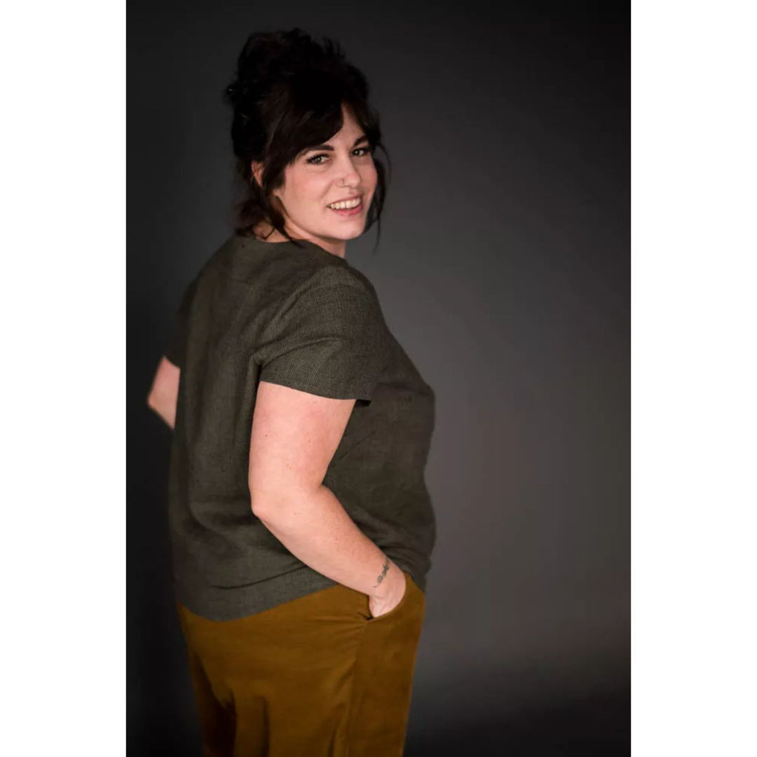 Woman wearing a green shirt and brown pants against a dark background