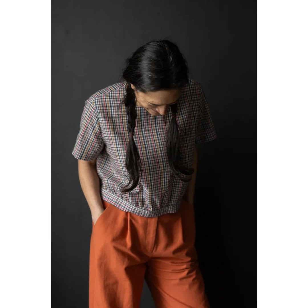 Person wearing a plaid shirt and orange pants against a dark background