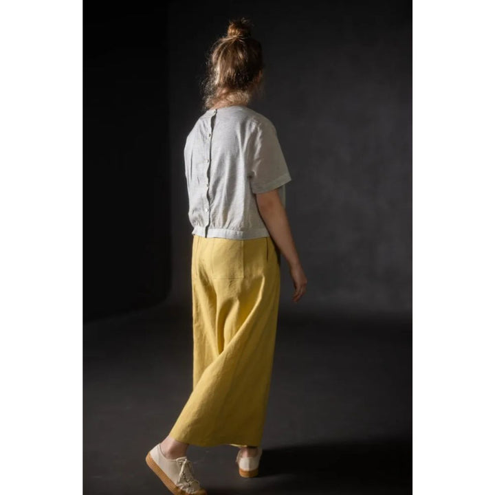 Person wearing a light-colored shirt and yellow pants against a dark background