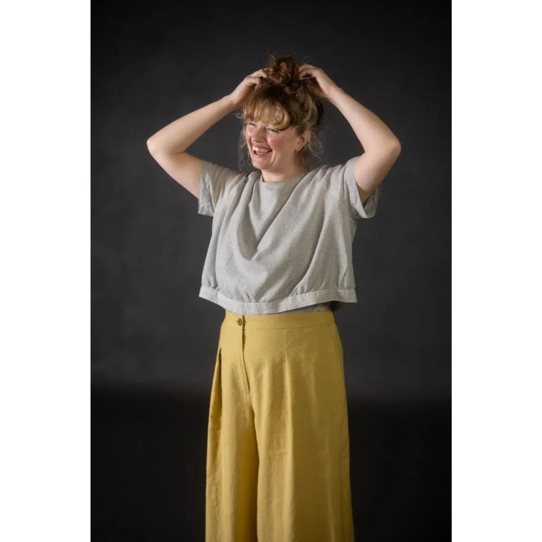 Person wearing a gray top and yellow pants against a dark background