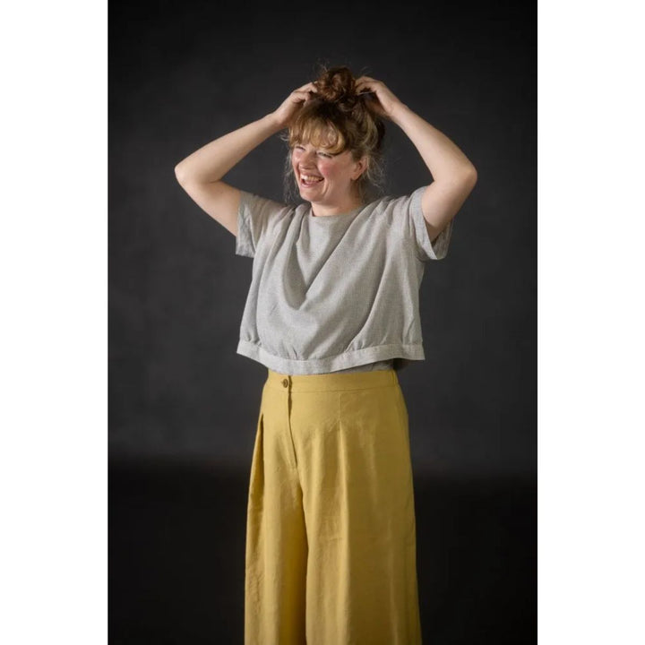 Person wearing a gray top and yellow pants against a dark background