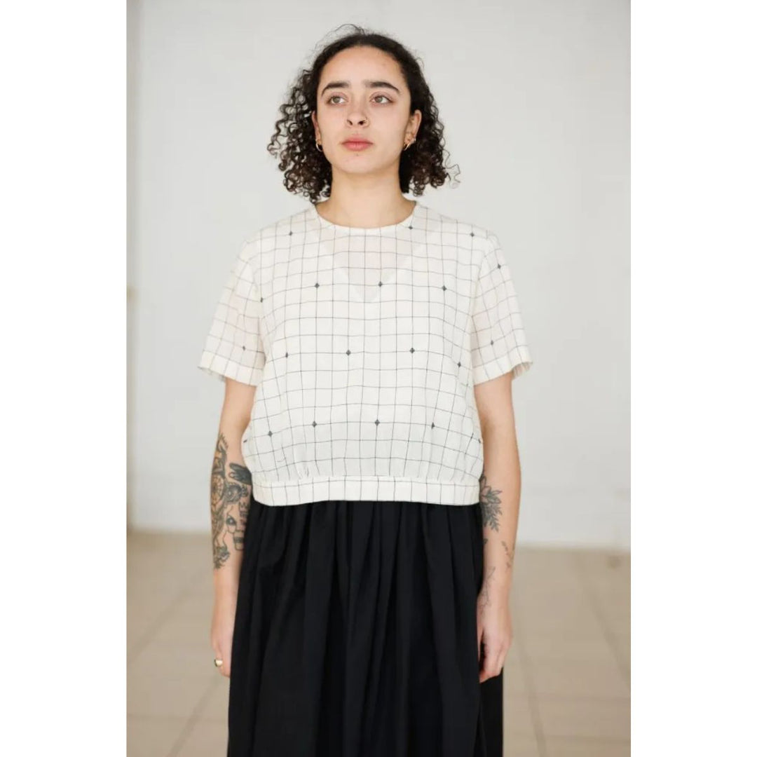 Person wearing a white grid-patterned top and black skirt against a plain background