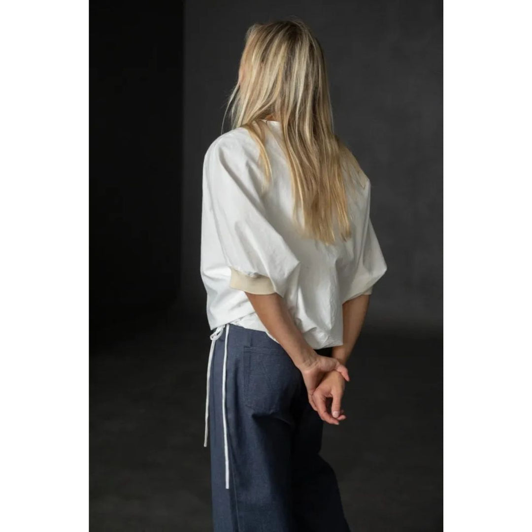 Person wearing a white shirt and dark pants against a dark background