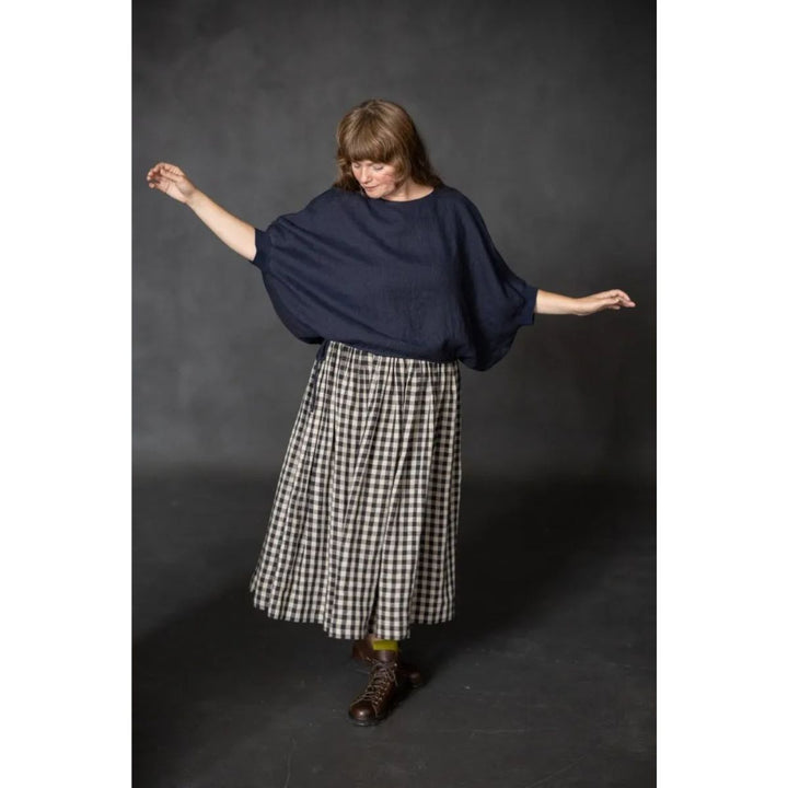 Woman wearing a navy blue top and checkered skirt against a dark background