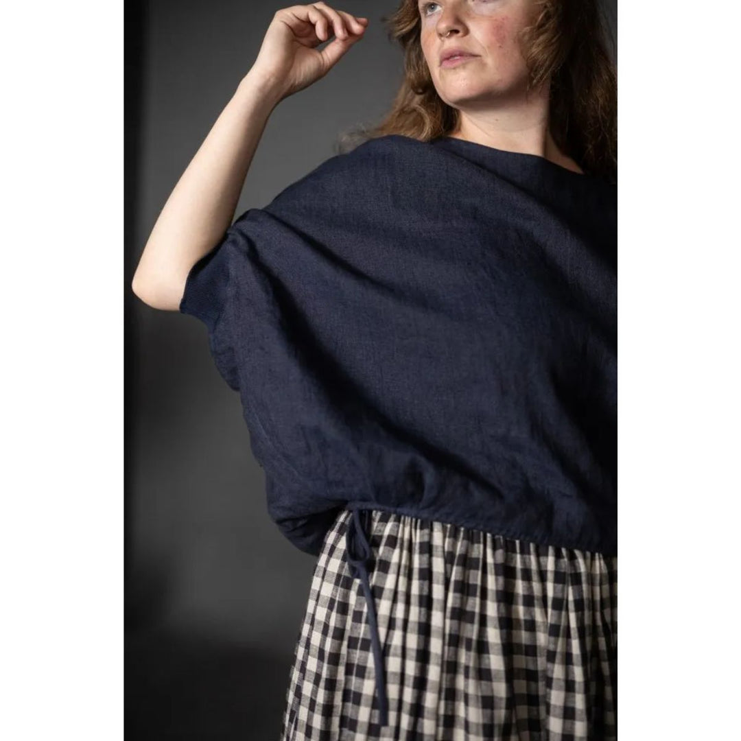 Woman wearing a navy blue sweater over a plaid skirt against a dark background