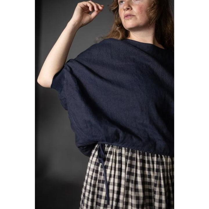 Woman wearing a navy blue sweater over a plaid skirt against a dark background