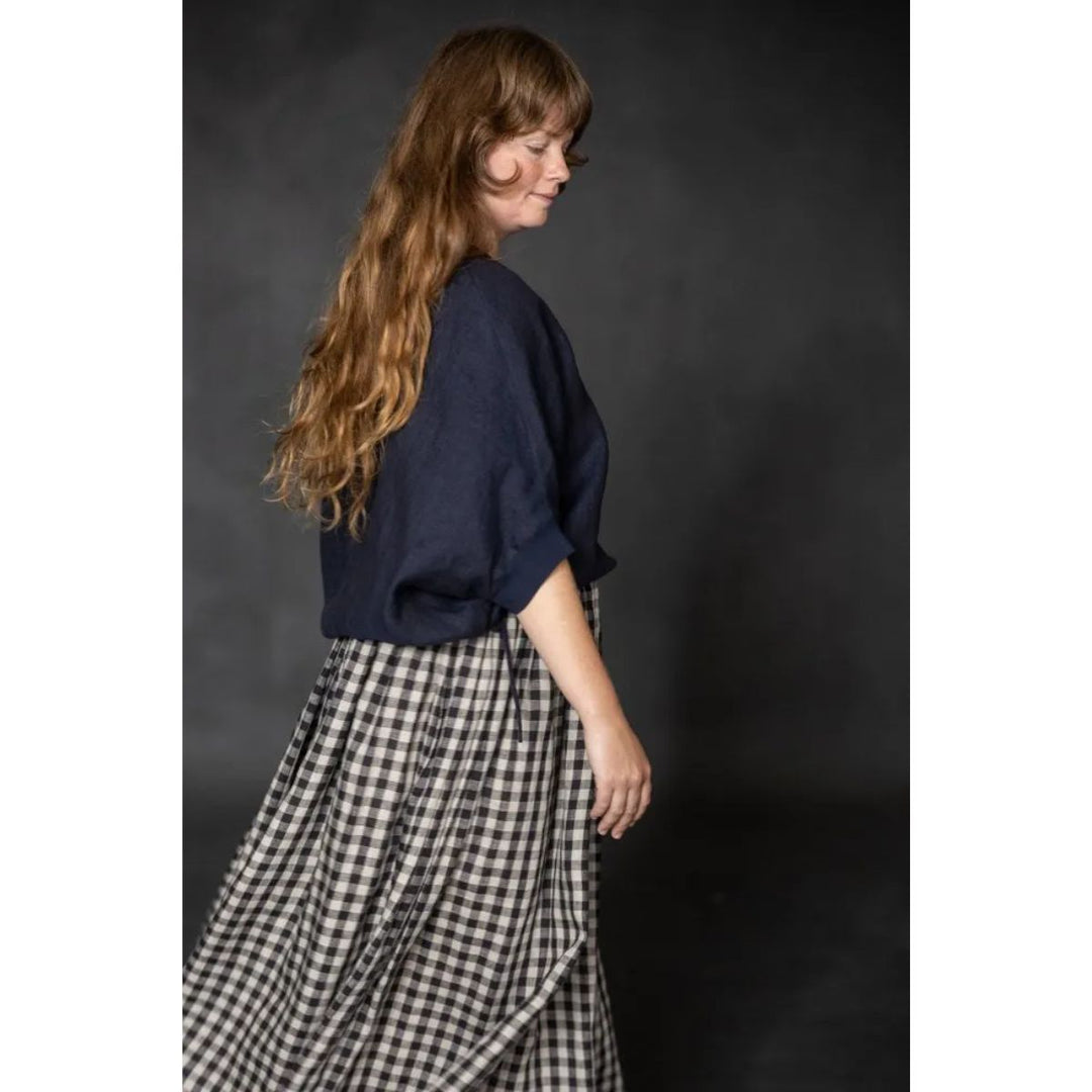 Woman wearing a navy top and checkered skirt against a dark background