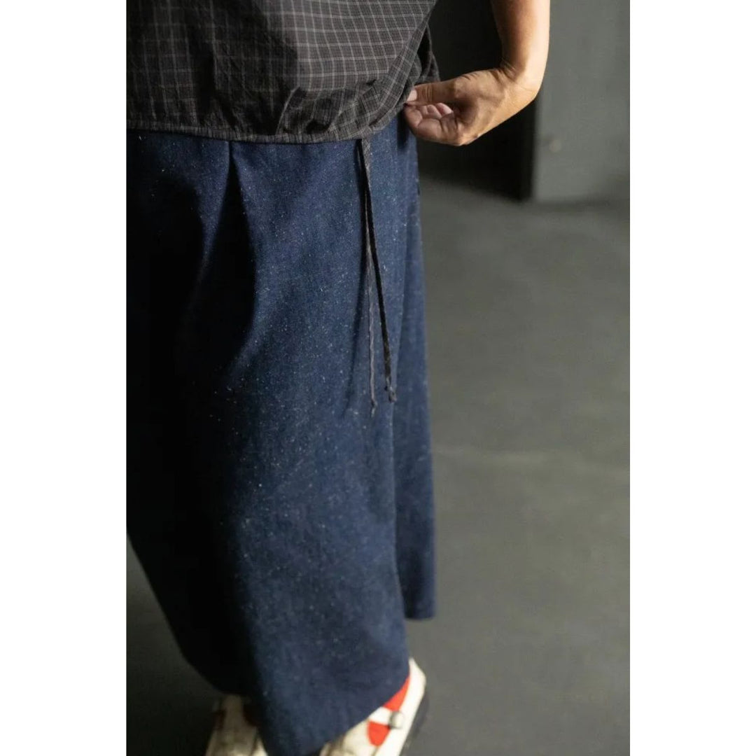 Person wearing dark blue pants with a checkered shirt on a plain background