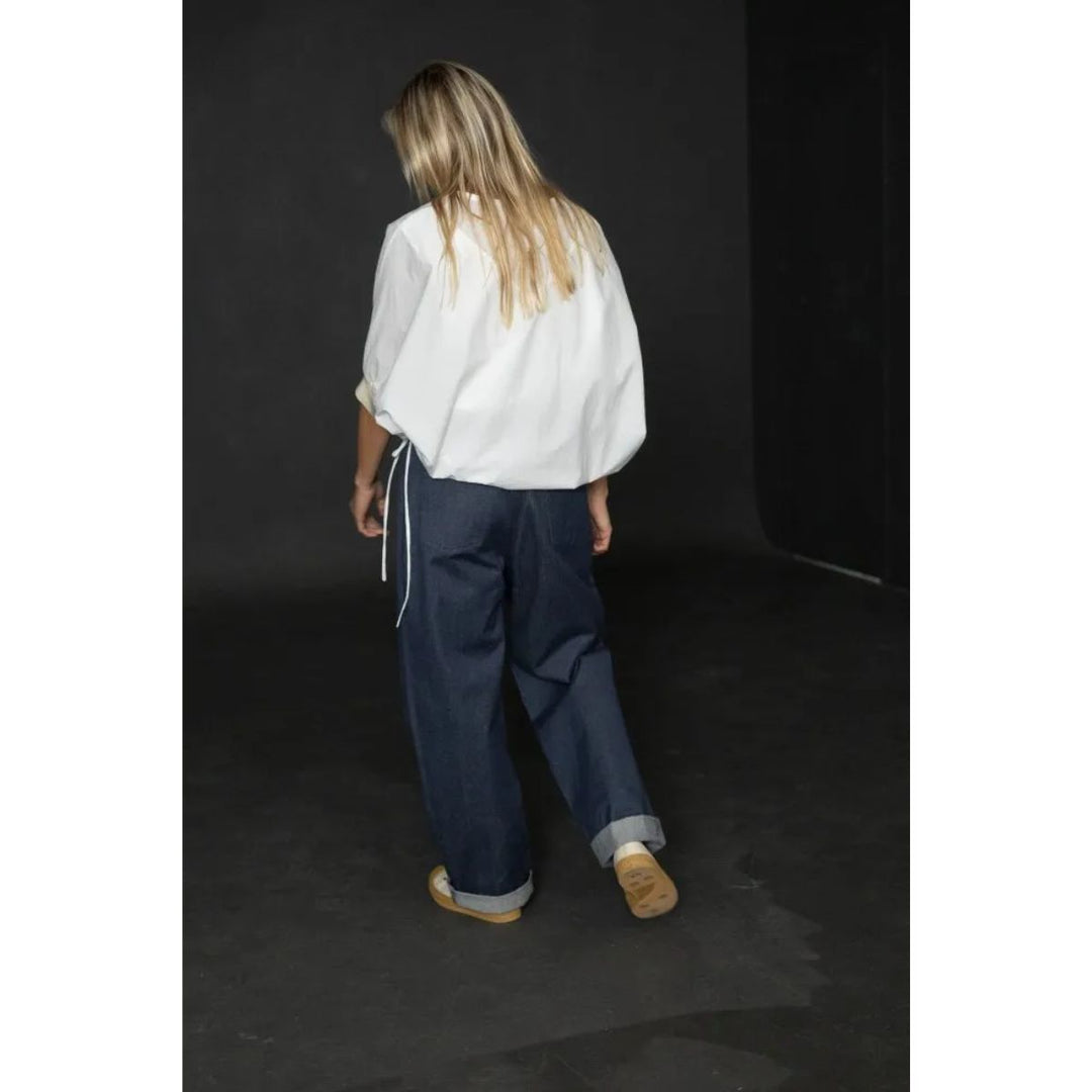 Person wearing a white shirt and blue pants against a dark background