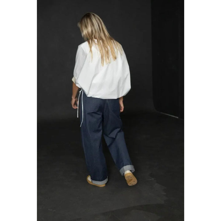 Person wearing a white shirt and blue pants against a dark background