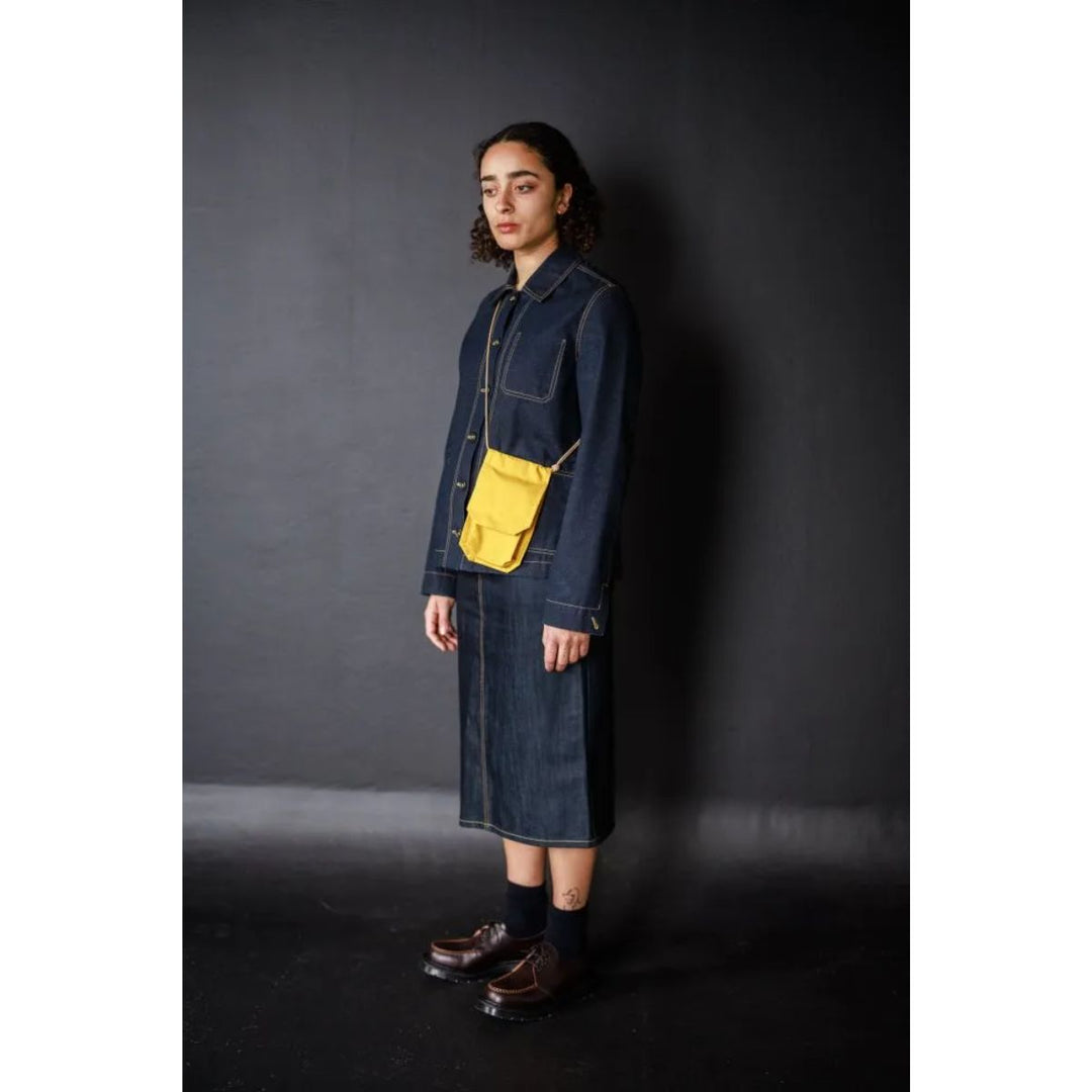 Person wearing a denim outfit with a yellow pocket against a dark background