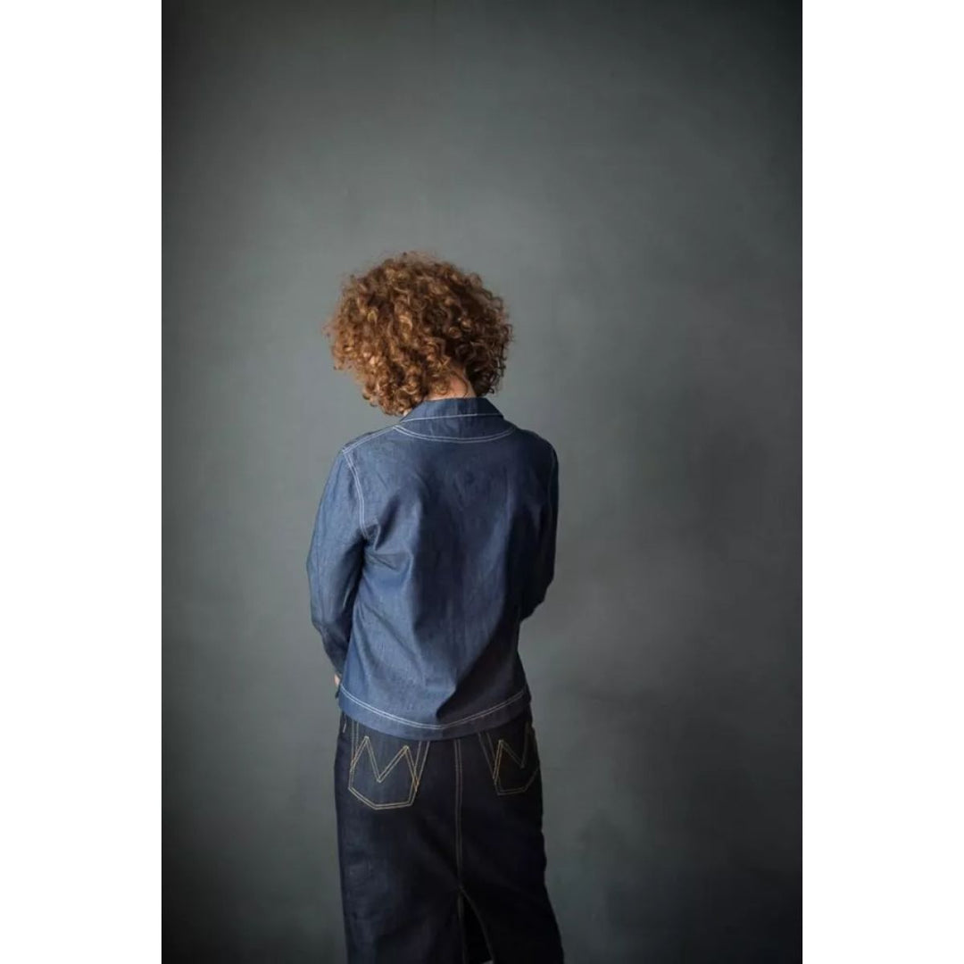 Person wearing a blue denim jacket and dark pants against a gray background