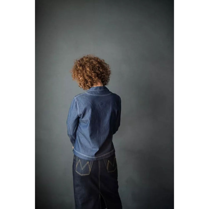 Person wearing a blue denim jacket and dark pants against a gray background