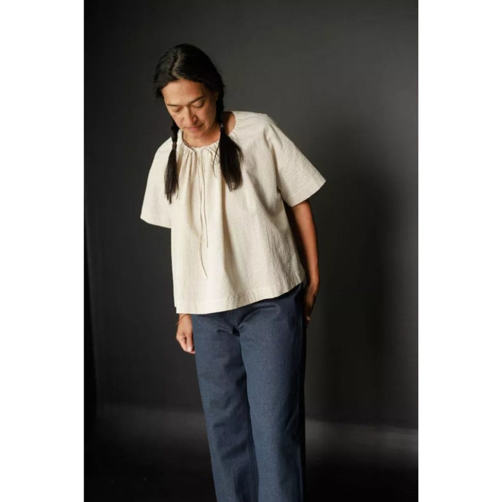 Person wearing a white blouse and blue pants against a dark background