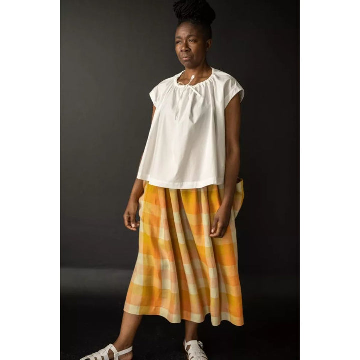 Woman wearing a white top and orange plaid skirt against a dark background