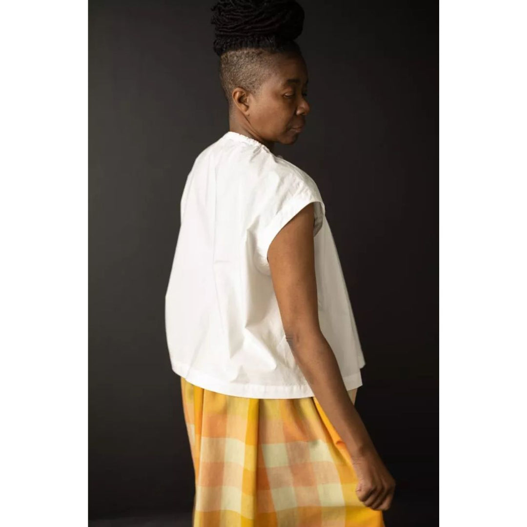 Woman wearing a white top and yellow plaid skirt against a dark background