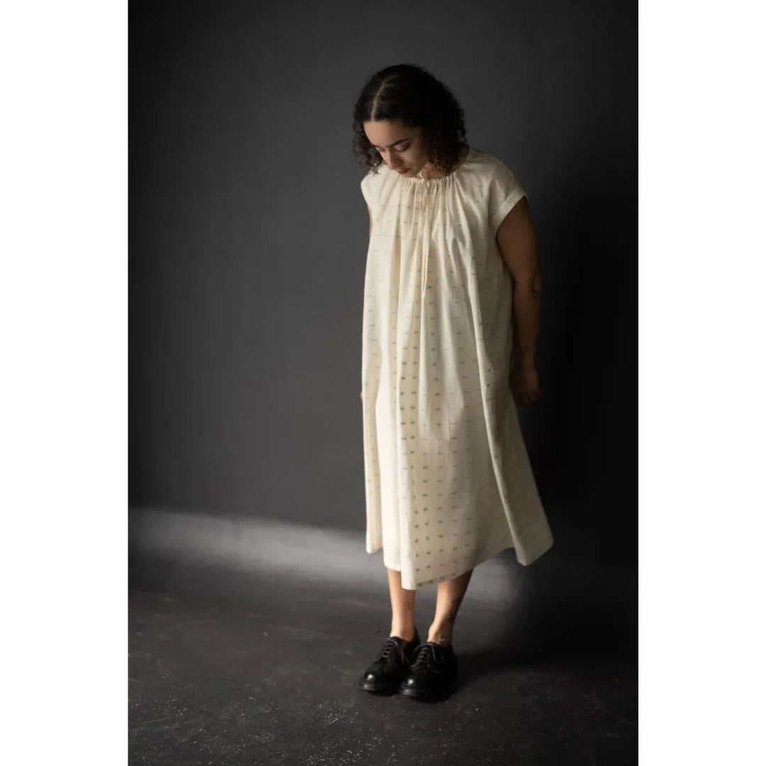 Woman wearing a white dress with a subtle pattern against a dark background