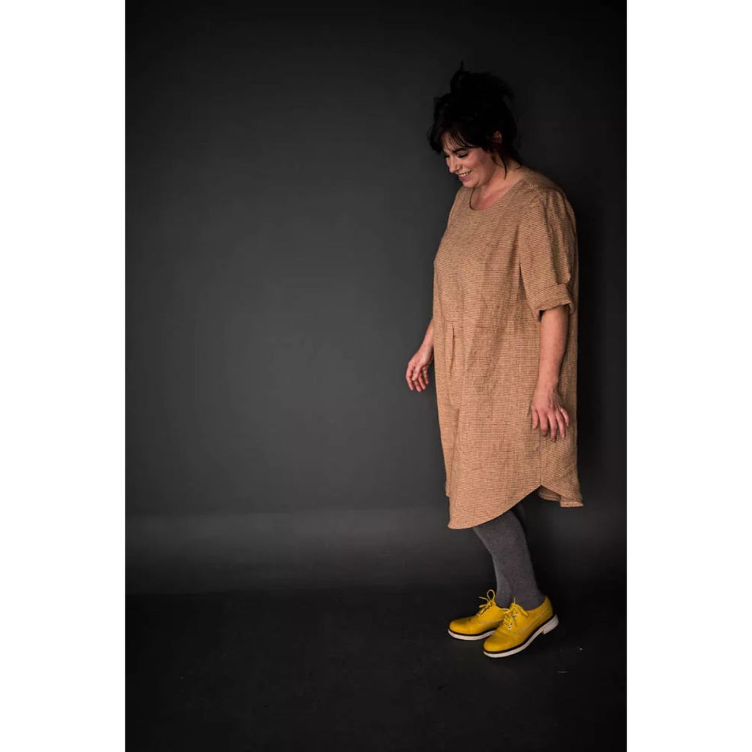 Woman wearing a beige dress with yellow shoes against a dark background