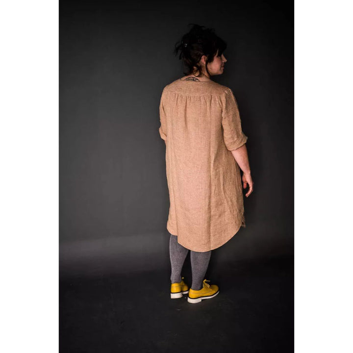 Person wearing a long beige dress against a dark background