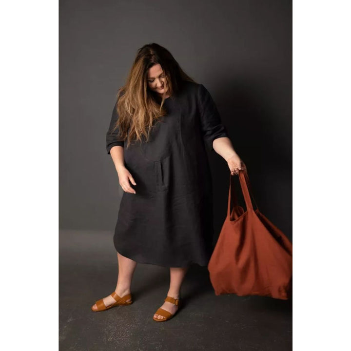 Woman in a black dress holding a brown bag against a dark background