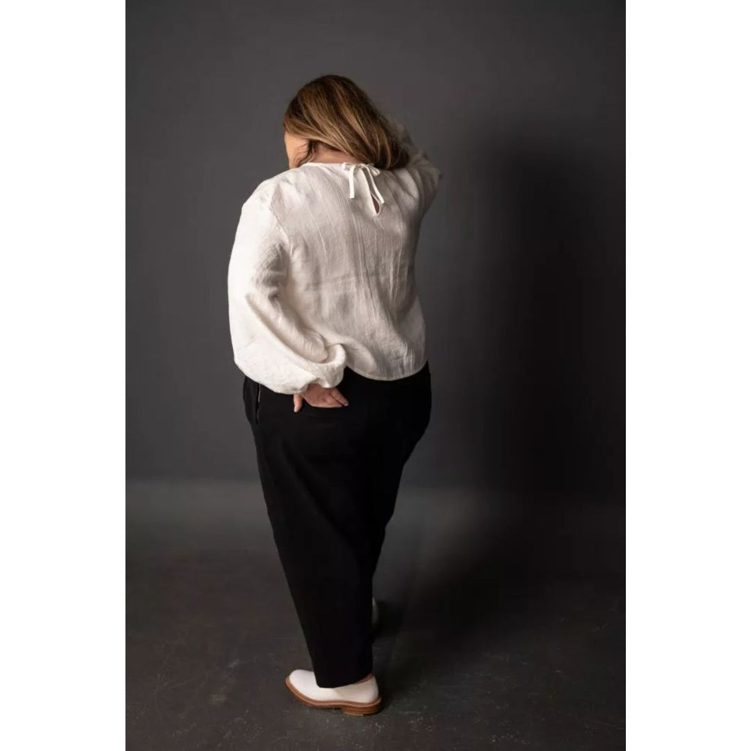 Person wearing a white blouse and black pants against a dark background