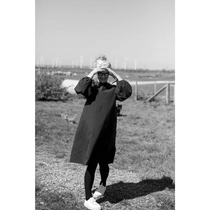 Person in a long coat standing outdoors with wind turbines in the background