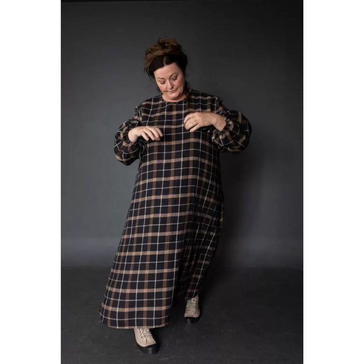 Person wearing a long plaid dress against a dark background