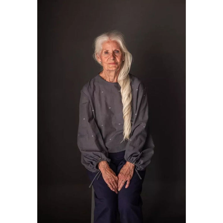 Woman with long white hair wearing a dark gray sweatshirt against a black background