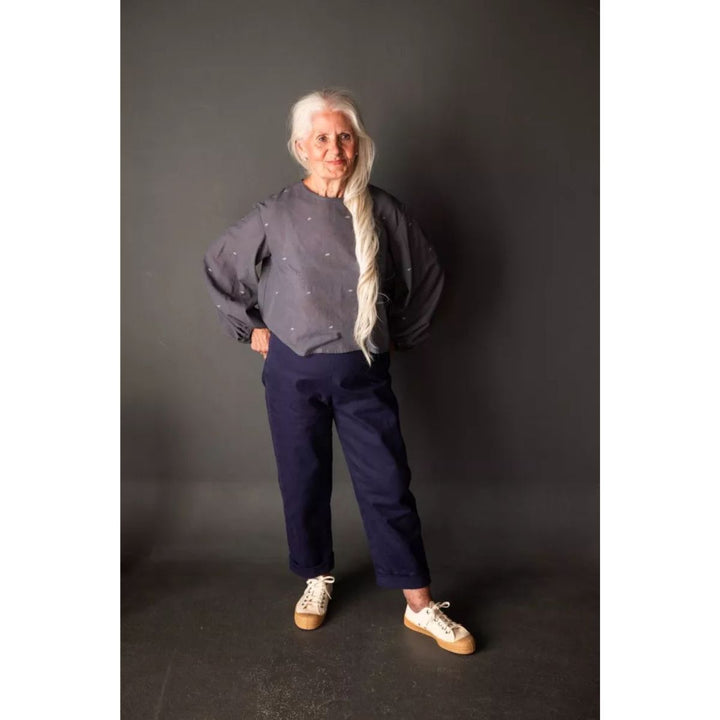 Person wearing a dark gray sweater and navy pants against a black background