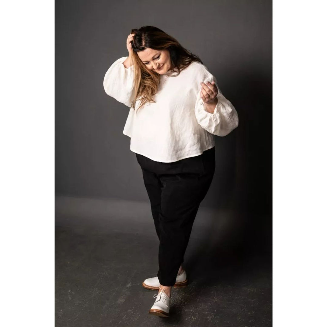 Woman wearing a white blouse and black pants against a dark background