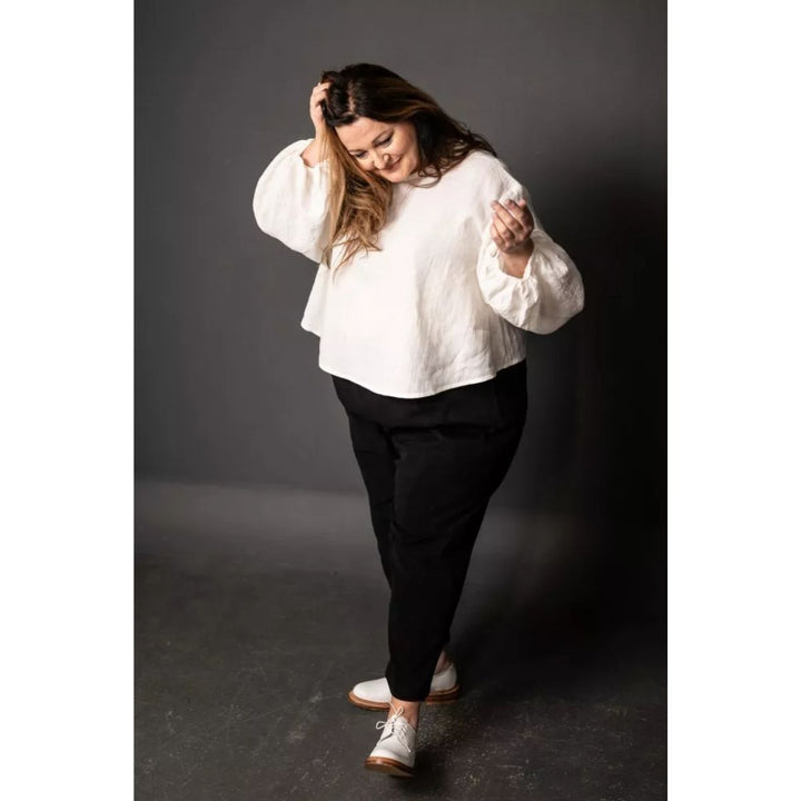 Woman wearing a white blouse and black pants against a dark background