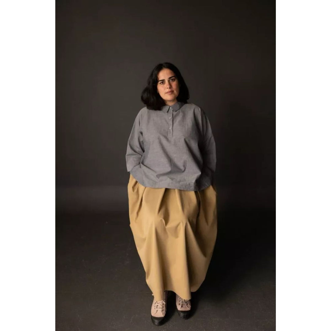 Woman wearing a gray sweater and beige pants against a dark background