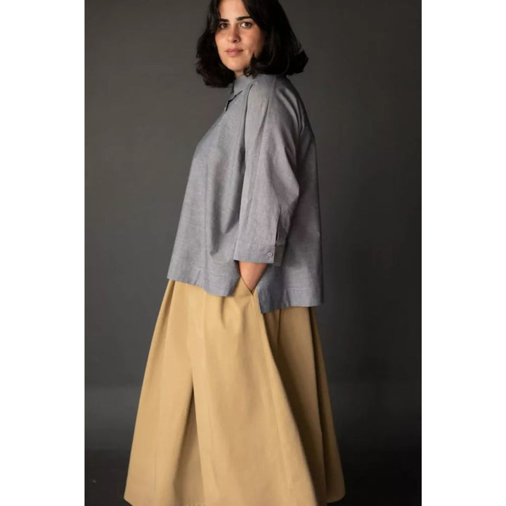 Woman wearing a gray top and beige pants against a dark background