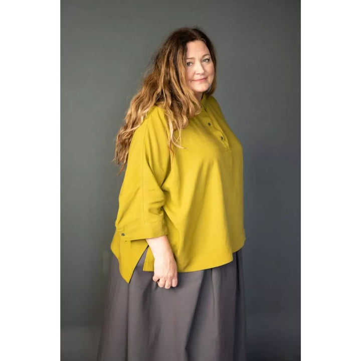 Woman wearing a mustard yellow shirt and gray pants against a gray background