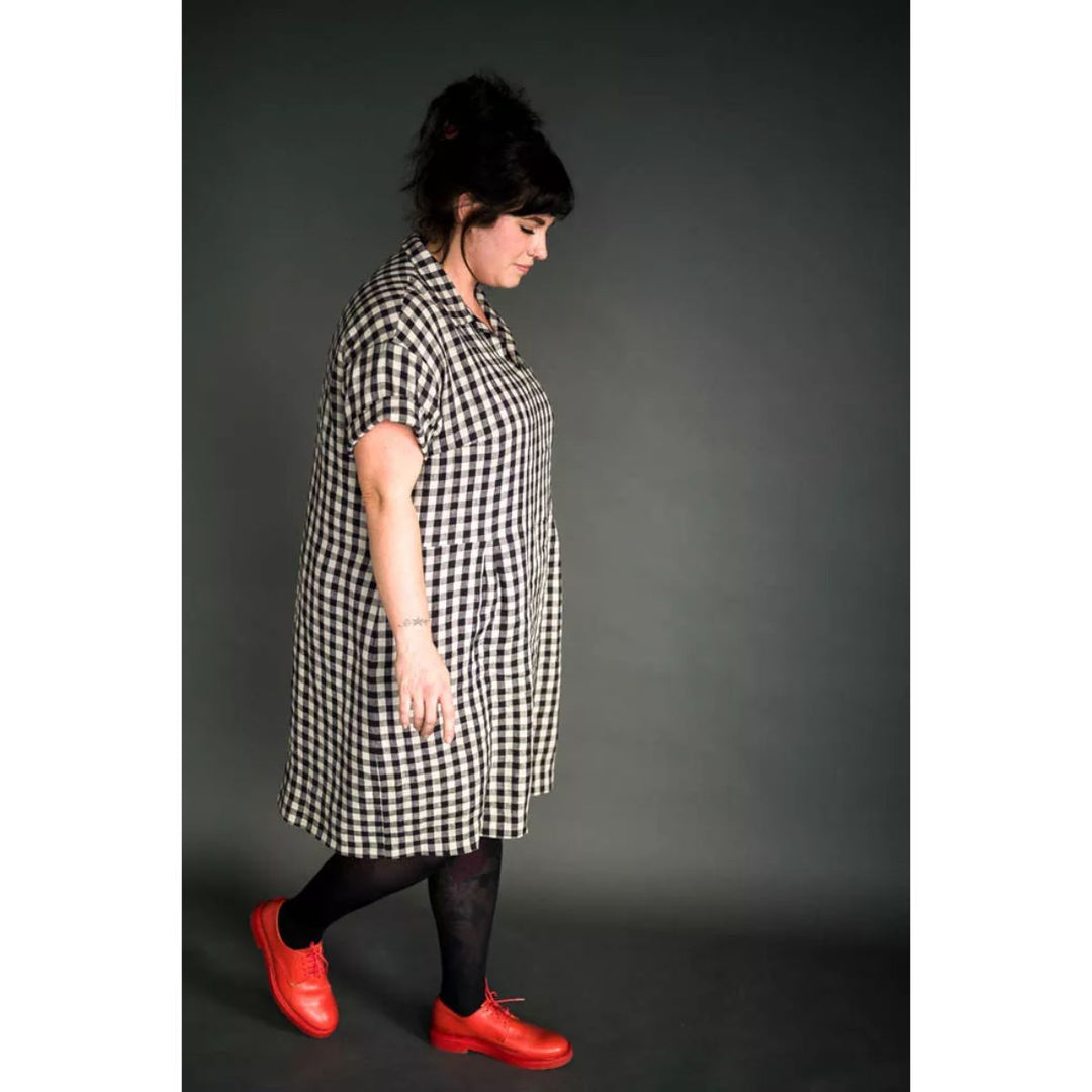 Person wearing a black and white checkered dress with red shoes on a gray background