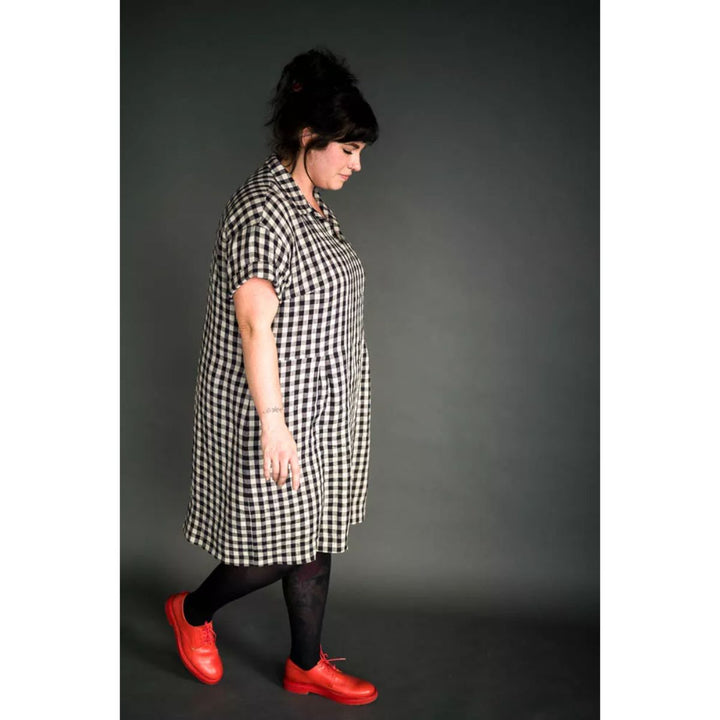 Person wearing a black and white checkered dress with red shoes on a gray background