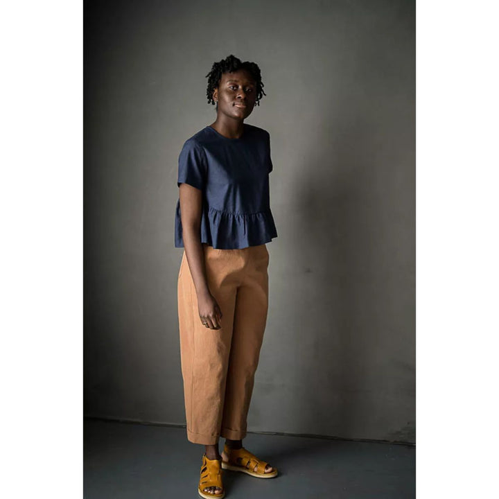 Woman wearing a blue top and brown pants against a dark background