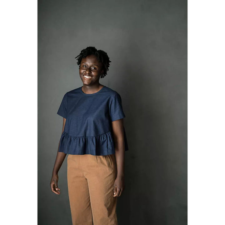 Woman wearing a blue top and brown pants against a dark background
