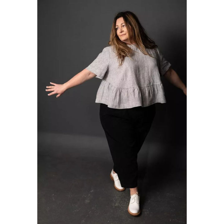 Woman wearing a light gray top and black pants on a dark background