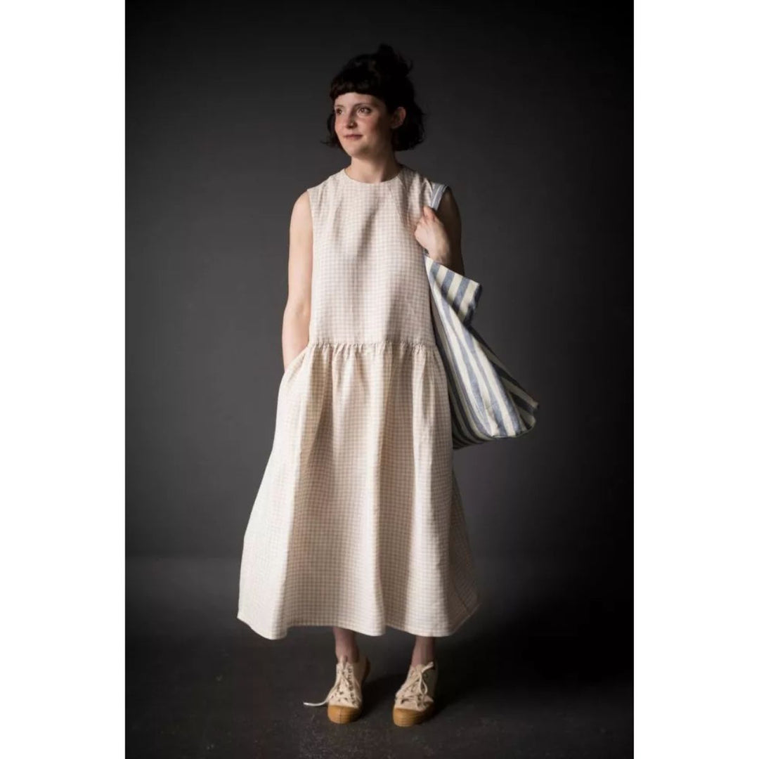 Woman wearing a beige checkered dress holding a striped bag against a dark background