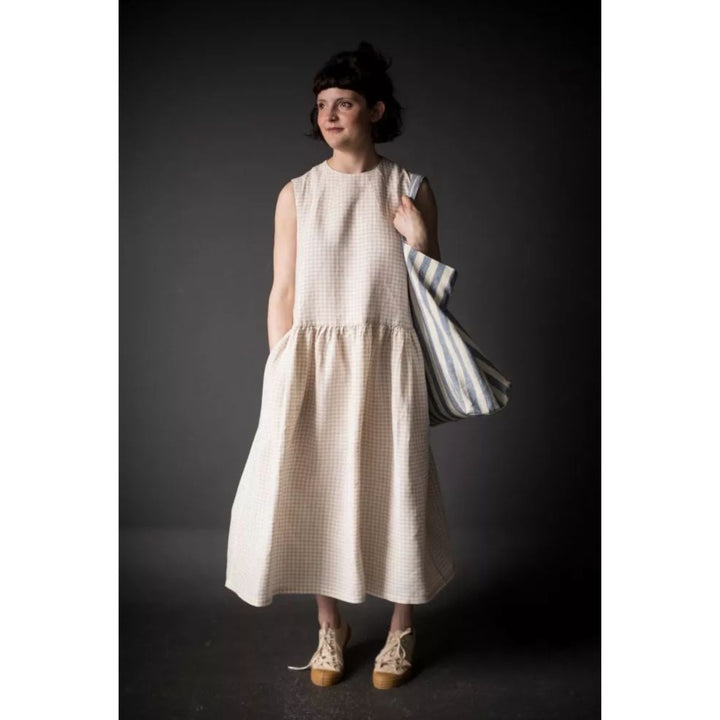 Woman wearing a beige checkered dress holding a striped bag against a dark background