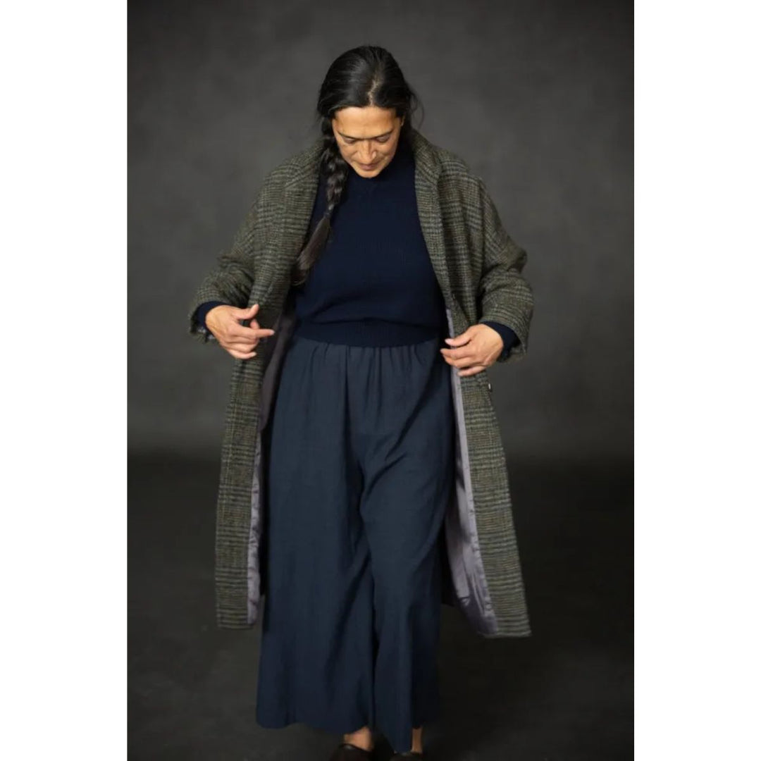 Person wearing a long green coat over a navy outfit against a dark background