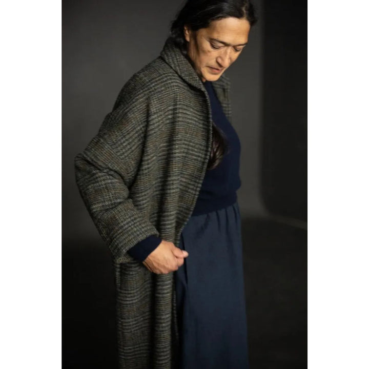 Person wearing a dark green checkered coat over a navy outfit against a dark background