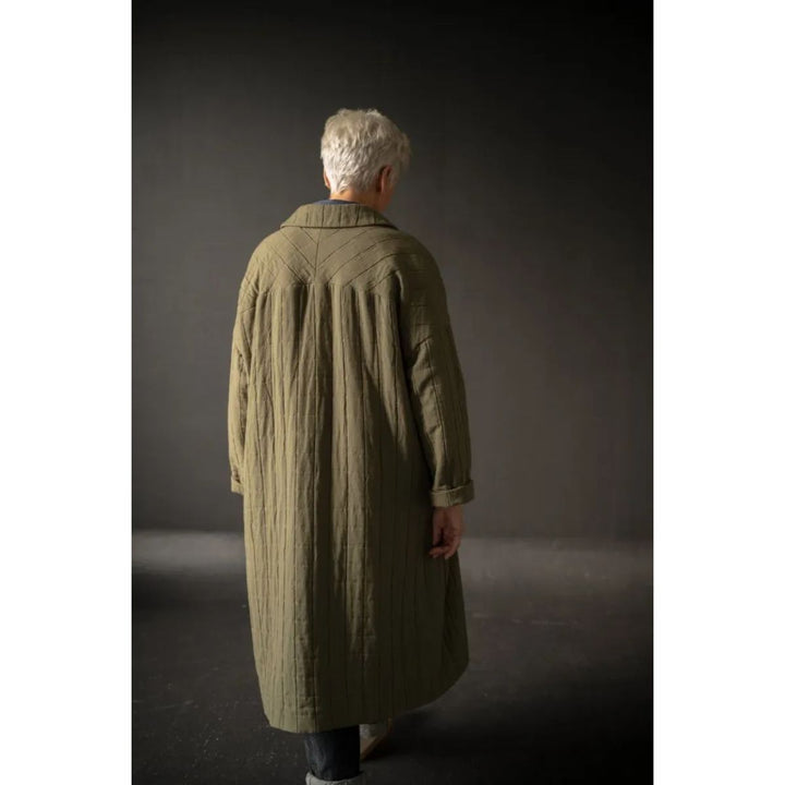 Person wearing a long olive green coat against a dark background