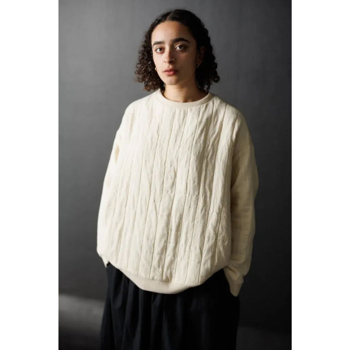 Person wearing a white cable knit sweater against a dark background